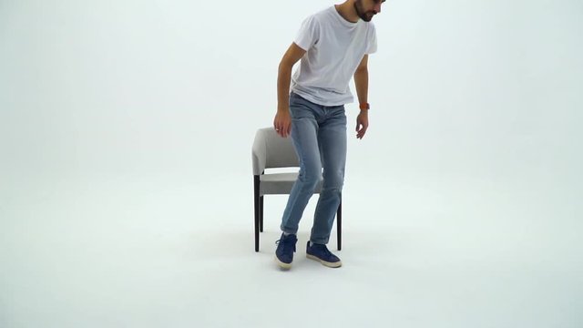 Handsome Man In White Tshirt And Chair On A White Background. Man Gets Up From The Chair And Going Away.