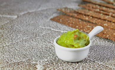 Guacamole in presentation bowl with crispy rye chips on light surface. Close up.