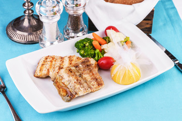 Mediterranean dish, European cuisine. Grilled pieces of fish, served with cooked vegetables - broccoli, cauliflower, cherry tomatoes and lemon