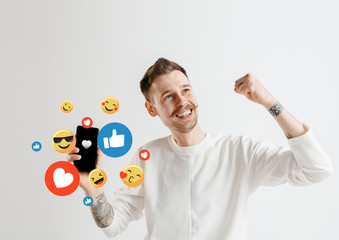 Social media interactions on mobile phone. Internet digital marketing, Chating, commenting, liking. Smiles and icons above smartphone screen, that holding by young man on white studio background.