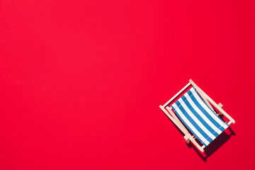 Deck chair with hard shadow on red paper background. Flat lay and copy space. Summer travel vacation concept. Minimal composition