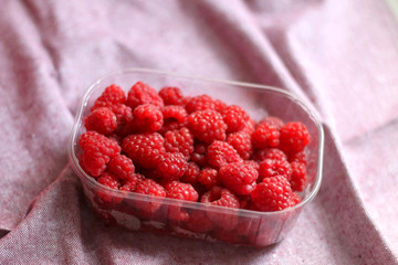 Fresh raspberries in a container. Selective focus, pink background.