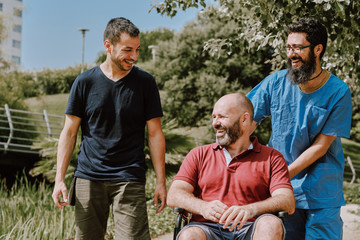 a man on wheelchair with his assistant and a friend - outdoor