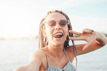 Carefree young woman with african braids making selfie on beach, summer vacation time