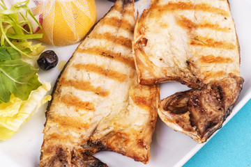 European cuisine, Mediterranean dish. steak of river fish with white meat, served with vegetables, lemon and arugula and tomato salad