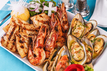 European cuisine, Mediterranean dish. Plate with assorted sea grill. Fried fish, king prawns with lemon, mussels with oyster sauce, colmar rings, crab meat