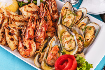 European cuisine, Mediterranean dish. Plate with assorted sea grill. Fried fish, king prawns with lemon, mussels with oyster sauce, colmar rings, crab meat
