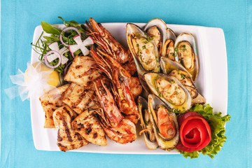 European cuisine, Mediterranean dish. Plate with assorted sea grill. Fried fish, king prawns with lemon, mussels with oyster sauce, colmar rings, crab meat
