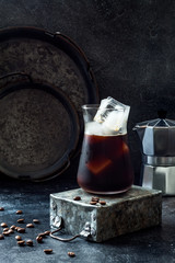 Cold refreshing iced coffee in a tall glass and coffee beans on dark background.