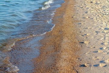 Fototapeta na wymiar Summer sunny sandy beach. Coastal waves. Many footprints in the sand.