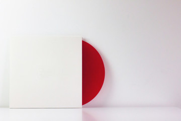 Red vinyl record, in its white box, with blank space to write. With white background. Minimalist photo.