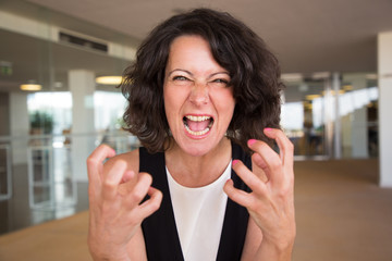 Crazy furious woman shouting at camera. Angry middle aged lady in casual screaming, making claw...