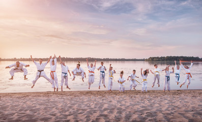 Funny jumping people. Karate kids team on sunset beach