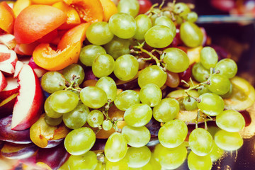 Closeup image of grape clusters near to platter with tasty parmesan cheese. Fresh juicy fruit bunch...