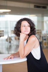 Pensive woman in casual waiting someone in cafeteria. Middle aged business lady leaning on cafe table and looking into distance. Woman in cafe concept