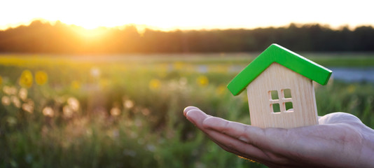 Wooden house in the hands in the sunset background. Real estate concept. Eco friendly home. Symbol...