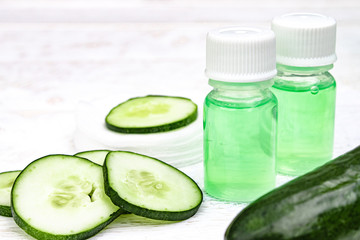 Sliced cucumber and a bottle of cucumber extract on a white wooden table and a white background. Liquid cosmetics for skin care.