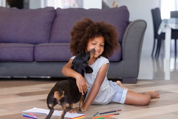 Little african girl playing with dachshund puppy on warm floor