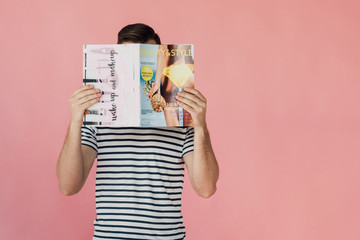 front view of man in striped t-shirt reading magazine isolated on pink - obrazy, fototapety, plakaty