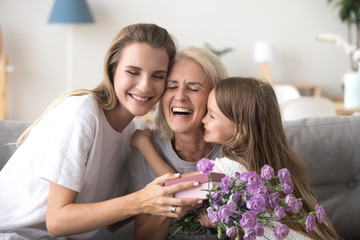 Daughter granddaughter and grandmother with gift box and flowers indoors