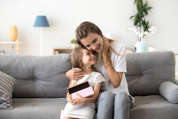 Loving mother hugging little daughter sitting together on sofa