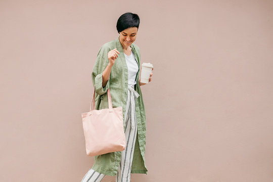 Woman with short hair holding reusable coffee cup and eco bag enjoying morning. Eco friendly concept.