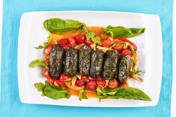 Uzbek cuisine, oriental cuisine. Dolma - Leaves of grapes, boiled rolls with meat, beef and rice. Served with vegetables - tomatoes, peppers, cucumbers and onions