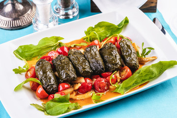 Uzbek cuisine, oriental cuisine. Dolma - Leaves of grapes, boiled rolls with meat, beef and rice. Served with vegetables - tomatoes, peppers, cucumbers and onions