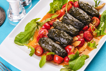 Uzbek cuisine, oriental cuisine. Dolma - Leaves of grapes, boiled rolls with meat, beef and rice. Served with vegetables - tomatoes, peppers, cucumbers and onions