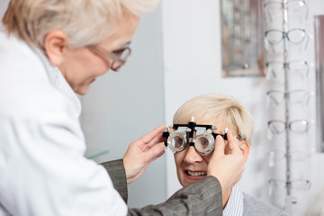 Close-up of smiling mature woman having eyesight exam and diopter measurement by a female optometrist at the ophthalmology clinic. Healthcare and medicine concept