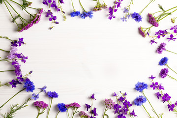 Beautiful blue and purple flowers frame flat lay on white wooden desk, copy space, top view