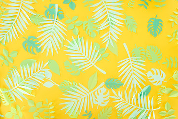 Fototapeta na wymiar top view of paper cut green tropical leaves on yellow bright background with copy space