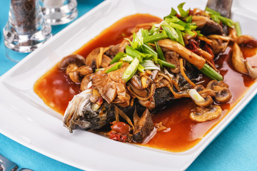 Seafood, Mediterranean cuisine, European dish. Fish stewed in tomato sauce with onion rings, mushrooms, herbs and vegetables. Caucasian national cuisine