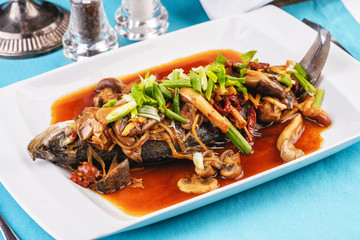 Seafood, Mediterranean cuisine, European dish. Fish stewed in tomato sauce with onion rings, mushrooms, herbs and vegetables. Caucasian national cuisine