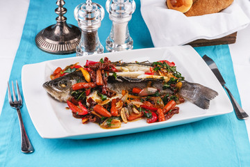 Seafood, Mediterranean cuisine, European dish. Whole fish baked with tomatoes with onion rings, red and green peppers, chili peppers, greens and vegetables. Caucasian national cuisine