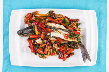 Seafood, Mediterranean cuisine, European dish. Whole fish baked with tomatoes with onion rings, red and green peppers, chili peppers, greens and vegetables. Caucasian national cuisine