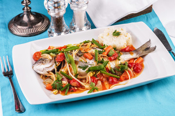 Seafood, Mediterranean cuisine. Baked sea fish with mushrooms, herbs, carrots, millers, cilantro, corn and onions. Caucasian national cuisine