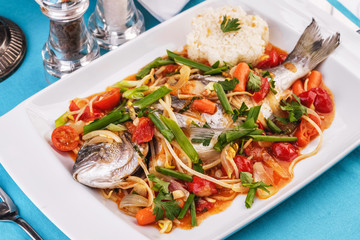 Seafood, Mediterranean cuisine. Baked sea fish with mushrooms, herbs, carrots, millers, cilantro, corn and onions. Caucasian national cuisine