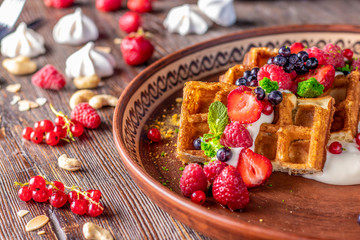 Homemade waffles with berry salsa and cream cheese in a plate on a wooden table, horizontal photo