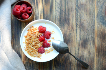 Delicious yogurt with granola and fresh raspberry in a bowl on a wooden background Healthy food concept Top view