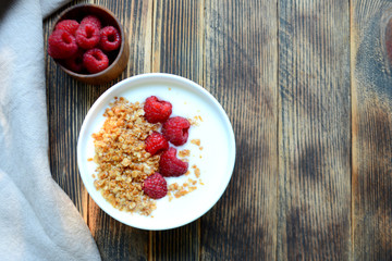 Delicious yogurt with granola and fresh raspberry in a bowl on a wooden background Healthy food concept Top view