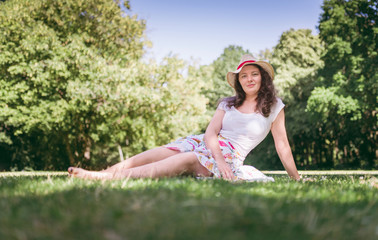 Naklejka na ściany i meble Summer portrait of young woman sitting on the grass, in sunny day. Beautiful, romantic woman.