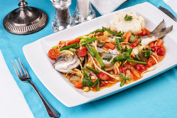 Seafood, Mediterranean cuisine. Baked sea fish with mushrooms, herbs, carrots, millers, cilantro, corn and onions. Caucasian national cuisine