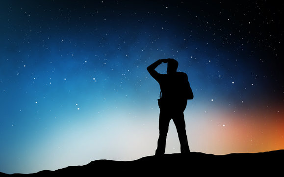 travel, tourism, hike and people concept - silhouette of traveler standing on edge and looking far away over starry night sky or space background