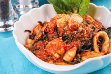 Mediterranean dish, Georgian recipe. Black pasta with shrimps, crab meat, seafood, squid rings, basil, greens and cheese.