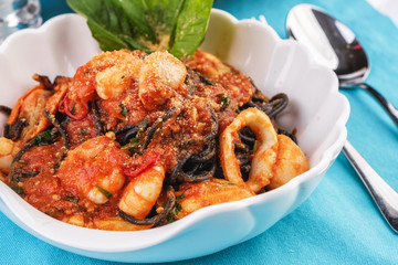 Mediterranean dish, Georgian recipe. Black pasta with shrimps, crab meat, seafood, squid rings, basil, greens and cheese.