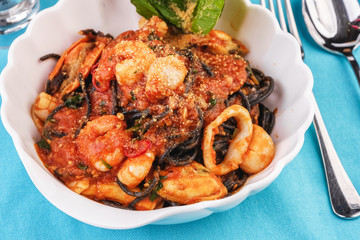 Mediterranean dish, Georgian recipe. Black pasta with shrimps, crab meat, seafood, squid rings, basil, greens and cheese.