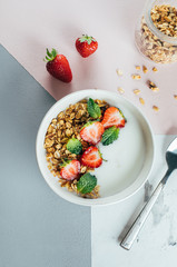 Flat lay Food Concept. Healthy breakfast. White nbowl with yogurt, homemade granola and strawberries on tricolor table background. Top view