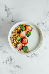 Healthy breakfast food minimal concept. Bowl with granola, yogurt and berries on white marble background. Top view, flat lay, copy space