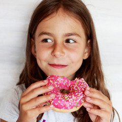 A beautiful little girl is eating a pink donut. Sweet treat